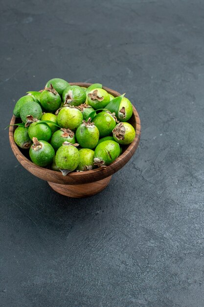 Bottom view fresh feijoas in wooden bowl on dark surface with copy space