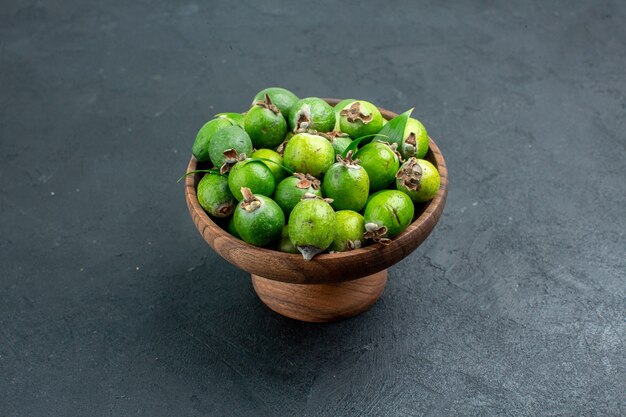 Bottom view fresh feijoas in wooden bowl on dark surface with copy space