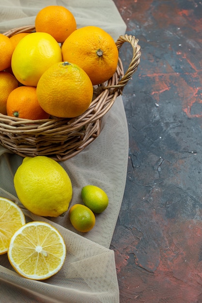 Bottom view fresh mandarins in wicker basket cut lemons cumcuat on tulle on dark red ground