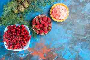 Free photo bottom view fresh raspberries currants and barberries in bowls pine tree branch small tart on blue table free space