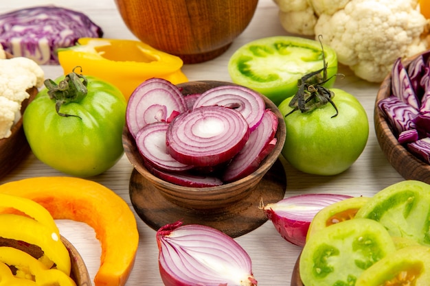 Foto gratuita vista dal basso verdure fresche peperoni pomodori verdi cavoli rossi cavolfiori zucche cipolle tagliate in ciotole su tavolo di legno bianco