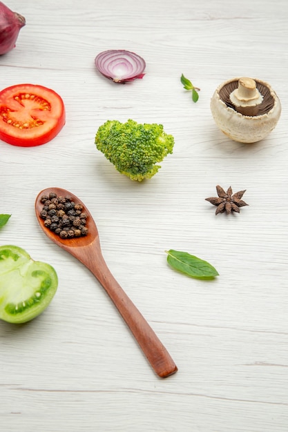 Bottom view fresh vegetables black pepper in wooden spoon mushroom red tomato onion broccoli mint leaves on grey table