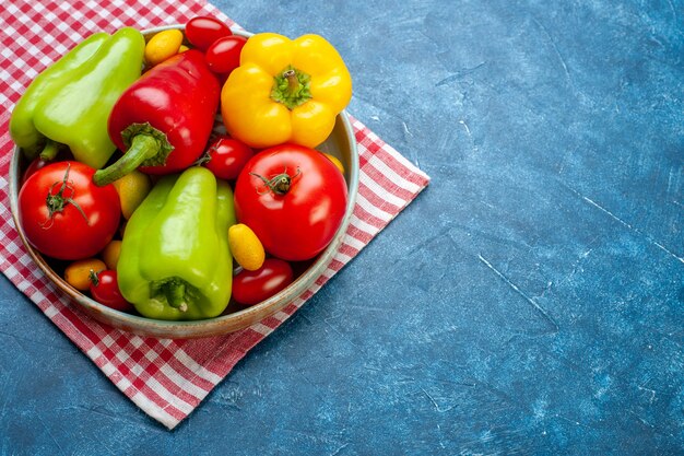 Bottom view fresh vegetables cherry tomatoes cumcuat different colors bell peppers tomatoes on platter on red and white checkered kitchen towel on blue table with copy place