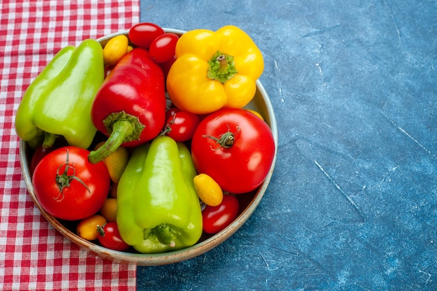 Bottom view fresh vegetables cherry tomatoes different colors bell peppers tomatoes cumcuat on platter on red and white checkered tablecloth on blue table free space stock photo