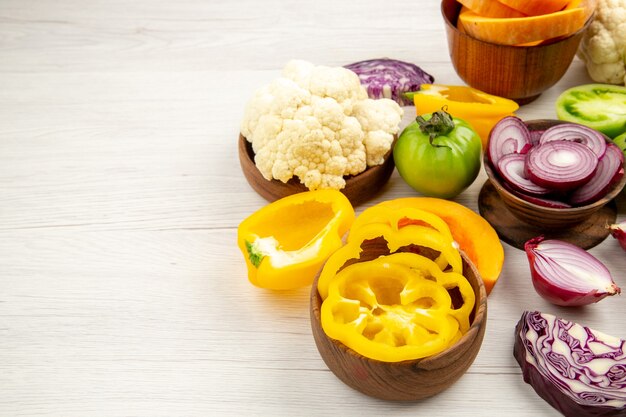 Bottom view fresh vegetables green tomato cut red cabbage cut bell peppers cauliflower cut onion in bowl on white wooden table free space