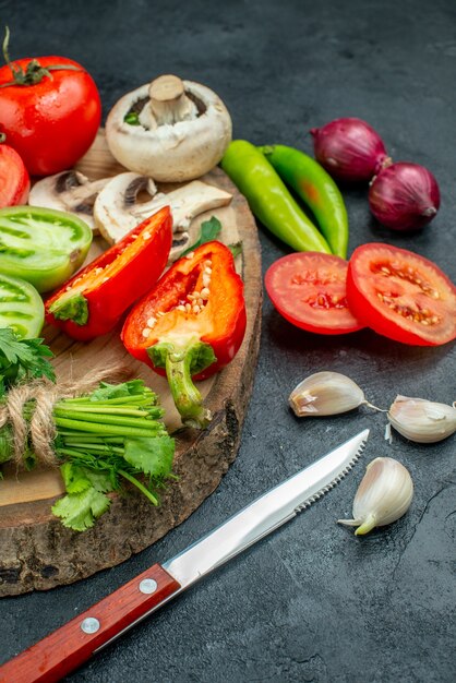 Bottom view fresh vegetables mushrooms red and green tomatoes bell peppers greens on rustic board hot peppers knife garlic on dark table