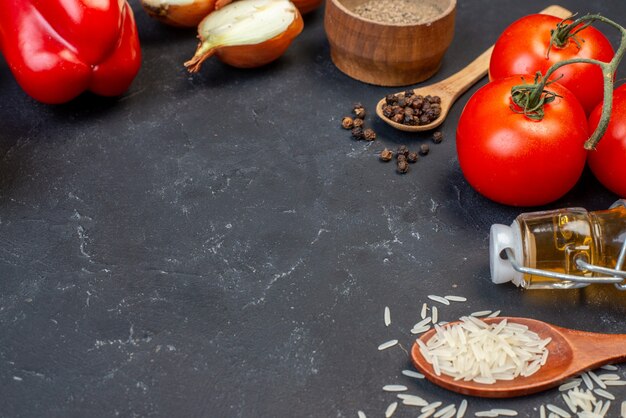 Вид снизу свежие овощи помидоры болгарский перец рис в деревянных ложках бутылка масла на черном столе место для копирования