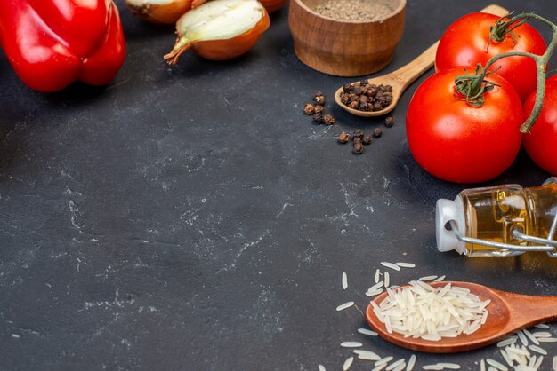 Bottom view fresh vegetables tomatoes bell pepper rice in wooden spoons oil bottle on black table copy place