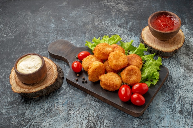 Bottom view fried cheese balls cherry tomatoes lettuce on cutting board sauce bowls on wood boards