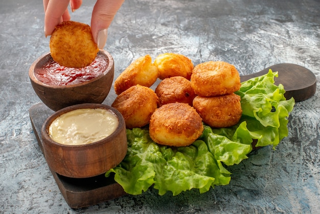 Bottom view fried cheese balls sauce bowls lettuce on cutting board cheese ball in female hand