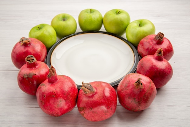 Bottom view green apples and pomegranates around round plate on white table