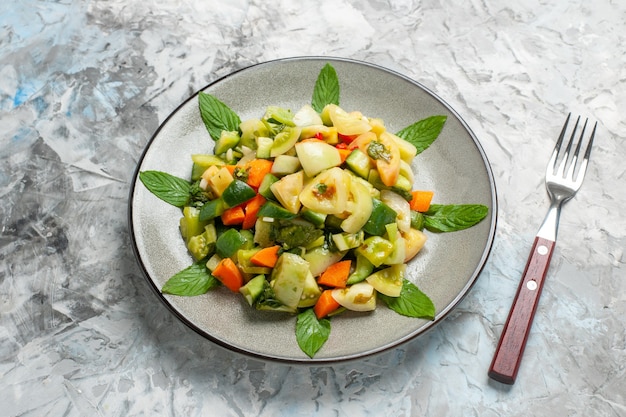 Bottom view green tomato salad on oval plate a fork on grey background