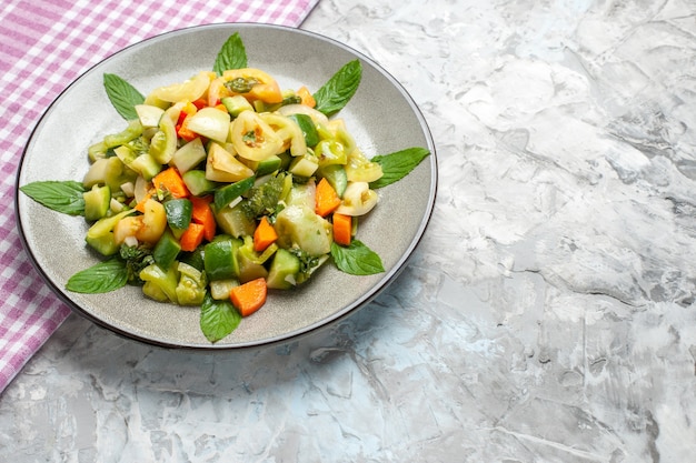 Bottom view green tomato salad on oval plate pink tablecloth on grey with free space