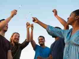 Free photo bottom view of happy people standing with bengal lights. smiling friends spending time together outdoor. concept of celebration