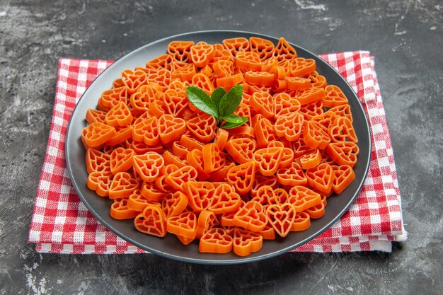 Красная итальянская паста в форме сердца на черной овальной тарелке на кухонном полотенце на темной поверхности, вид снизу
