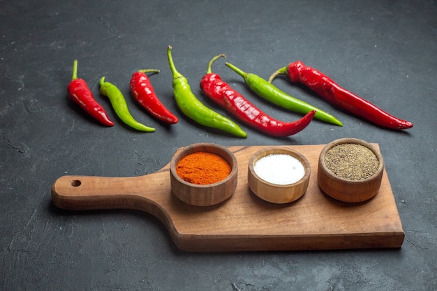 Free photo bottom view horizontal row green and red peppers different spices on cutting board on dark background