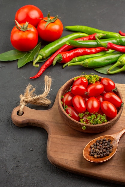 Vista dal basso peperoni rossi e verdi caldi e pomodori foglie di alloro una ciotola con pomodorini e pepe nero in un cucchiaio su un tagliere su fondo nero