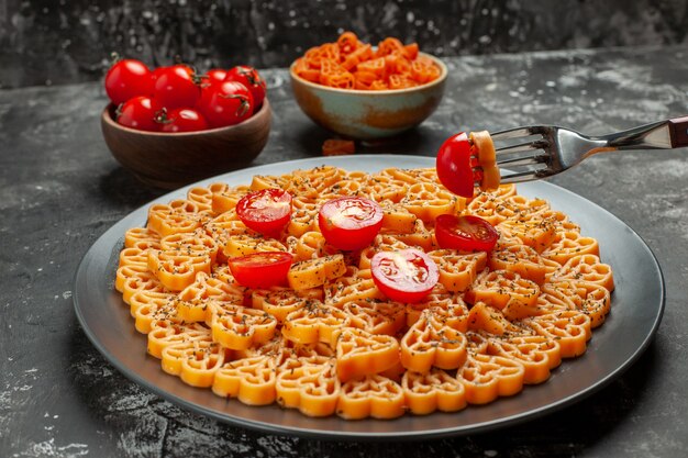 하단보기 이탈리아 파스타 마음은 타원형 접시 포크 체리 토마토와 회색 테이블에 그릇에 붉은 심장 파스타에 체리 토마토를 잘라