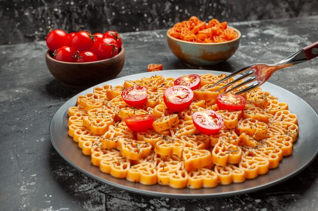 Вид снизу итальянские сердечки из макарон нарезанные помидоры черри на овальной тарелке, вилка, помидоры черри и макароны с красным сердцем в мисках на сером столе