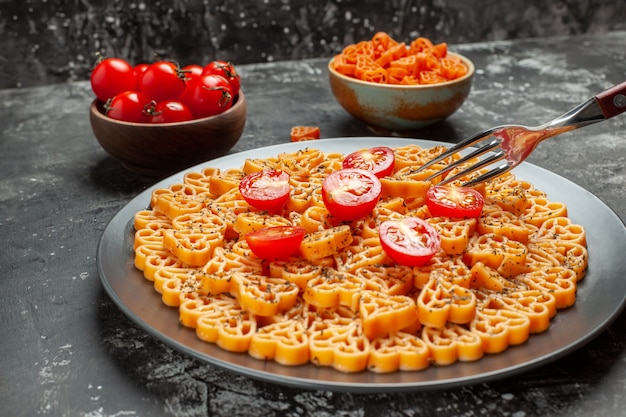 Bottom view italian pasta hearts cut cherry tomatoes on oval plate fork cherry tomatoes and red heart pasta in bowls on grey table
