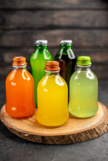 暗い木の表面の木製ボード上のボトルのさまざまな色のジュースの底面図