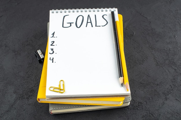 暗い背景のメモ帳鉛筆削り黒と黄色の鉛筆宝石クリップに書かれた目標の底面リスト