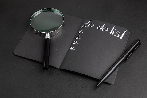 Вид снизу, чтобы сделать список, написанный на черной ручке блокнота lupa на черном столе