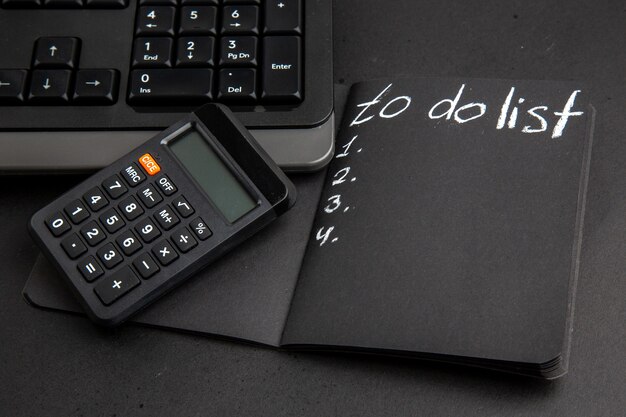 Bottom view to do list written on notepad calculator keyboard on black table