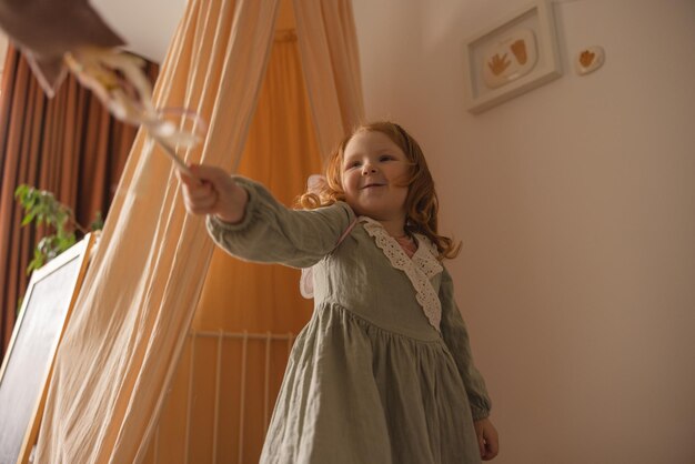 Bottom view of little caucasian cute baby girl with red hair plays with magic wand Child lifestyle concept