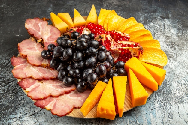 Bottom view meat slices cheese grapes and pomegranate on oval serving board on dark background