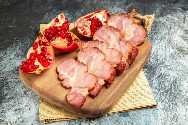 Bottom view meat slices cut pomegranate on cutting board on newspaper grey background