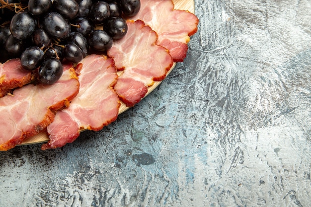 Bottom view meat slices grapes on oval serving board on dark