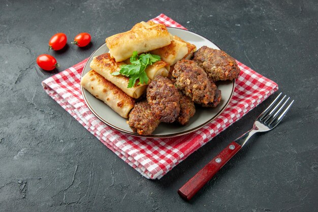 Bottom view meat stuffed blini and cutlets on round plate fork cherry tomatoes on table