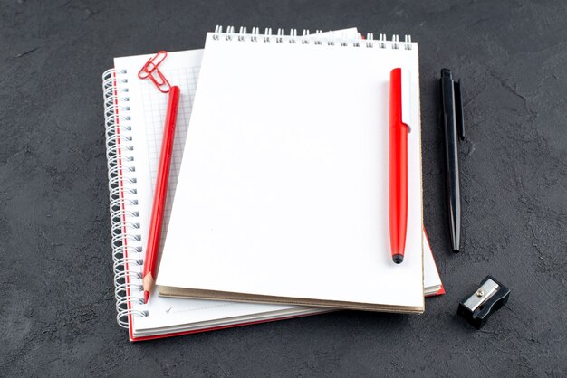 Bottom view office stuffs notepads red and black pens pencil sharpener on dark background