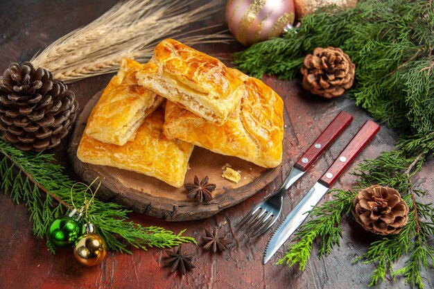 Bottom view penovani khachapuri on wood board pine tree branches and cones fork knife on dark red table