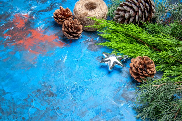 Bottom view pine tree branches with pinecones straw thread on blue-red background free space