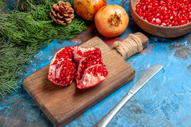 Bottom view pomegranate seeds in bowl dinner knife a cut pomegranate on chopping board tree branches on blue background