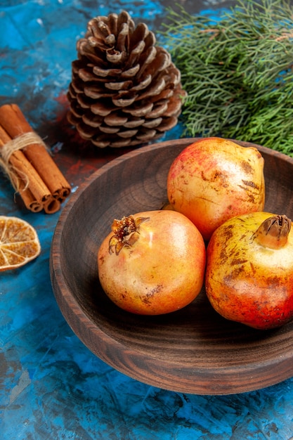 Free photo bottom view pomegranates on wooden plate pomegranate seeds in wooden bowl pine tree branch and cone dried lemon slice cinnamon on blue background