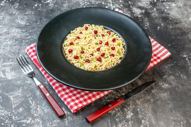底面図暗い丸皿のラーメン麺赤白市松模様のナプキン暗いテーブルの上のフォークとナイフ