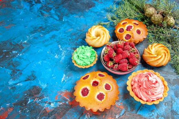 Bottom view raspberry cakes biscuits small tarts pinecones bowl with raspberries on blue table free space