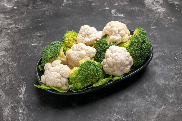 Bottom view raw broccoli and cauliflower on black oval plate on dark background