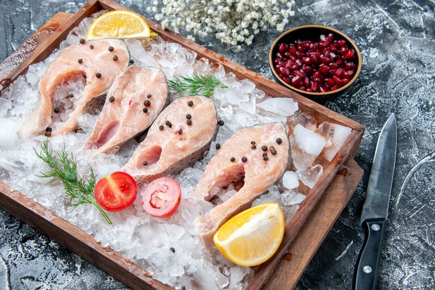 Bottom view raw fish slices with ice on wood board pomegranate seeds in small bowl knife on table