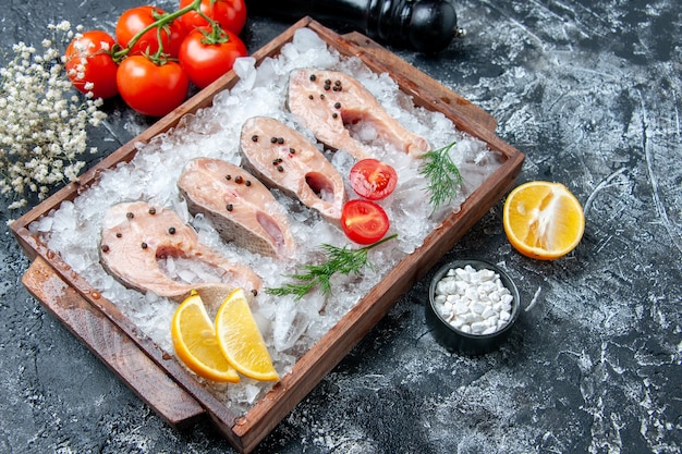Bottom view raw fish slices with ice on wood board tomatoes pepper grinder sea salt on table