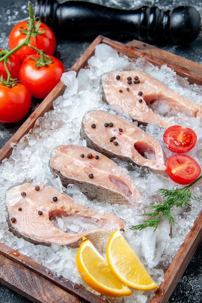 Bottom view raw fish slices with ice on wood board tomatoes pepper grinder on table