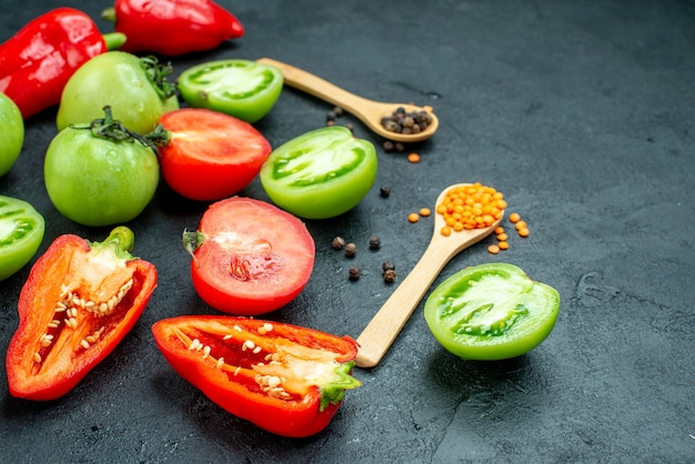 Bottom view red and green tomatoes cut bell peppers black pepper cozy red lentils in wooden spoons on dark table