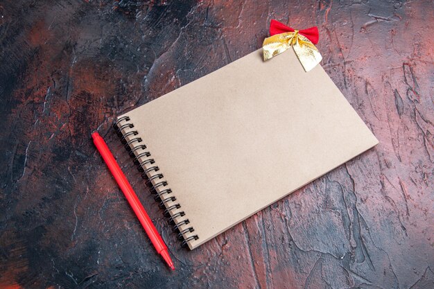 Bottom view red pen a notepad with small bow on dark red background