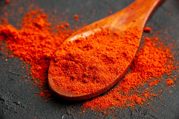 Bottom view red pepper powder on wooden spoon on black table