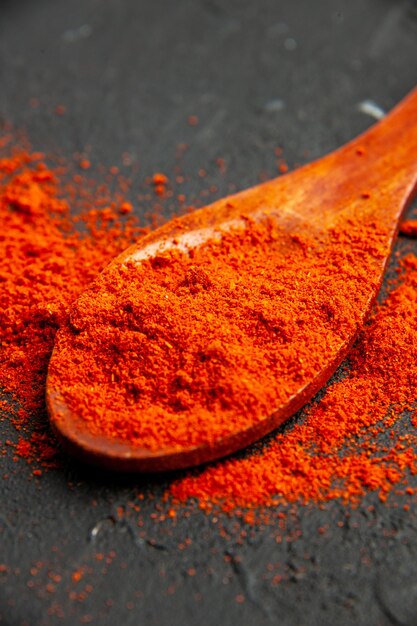 Bottom view red pepper powder on wooden spoon on dark surface