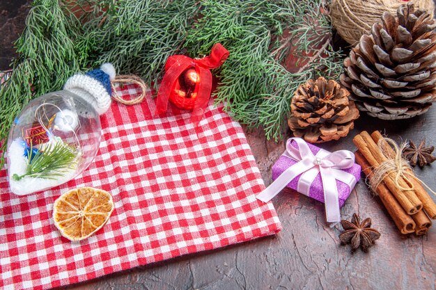 Bottom view red and white checkered tablecloth pine tree branches pinecones xmas gift cinnamon xmas tree toys anises on dark red background