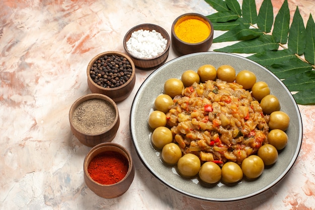 Free photo bottom view roasted eggplant salad on plate different spices in small bowls on nude table